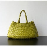 Green woven leather hobo bag with long handle, trapezoidal shape on black surface