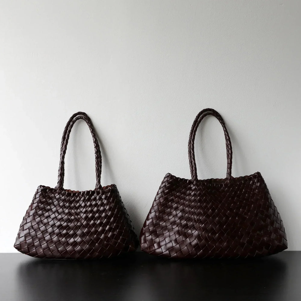Two dark brown woven leather hobo shoulder bags with long braided handles on black surface