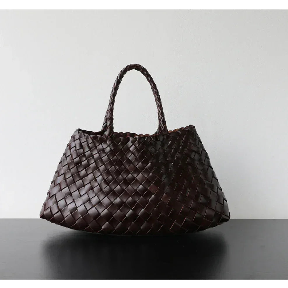 Dark brown woven leather hobo bag with long handle and trapezoidal shape on black surface