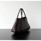 Brown woven leather hobo shoulder bag with braided handles on a black table