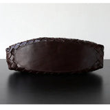 Bottom view of a dark brown full grain leather woven shoulder bag on a black table