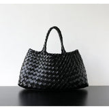 Woman holding black woven leather hobo bag with dual handles, stylish and trapezoidal shape black