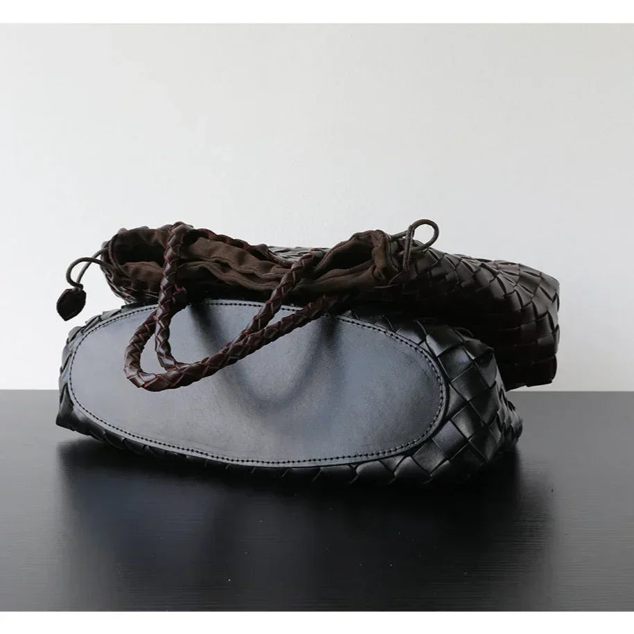 Woman holding black woven leather hobo bag with dual handles, stylish and trapezoidal shape black