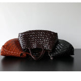 Three woven leather hobo bags in brown, black, and tan on a dark surface