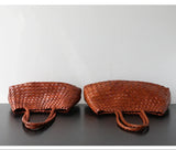 Two brown woven leather hobo shoulder bags with braided handles on a black surface