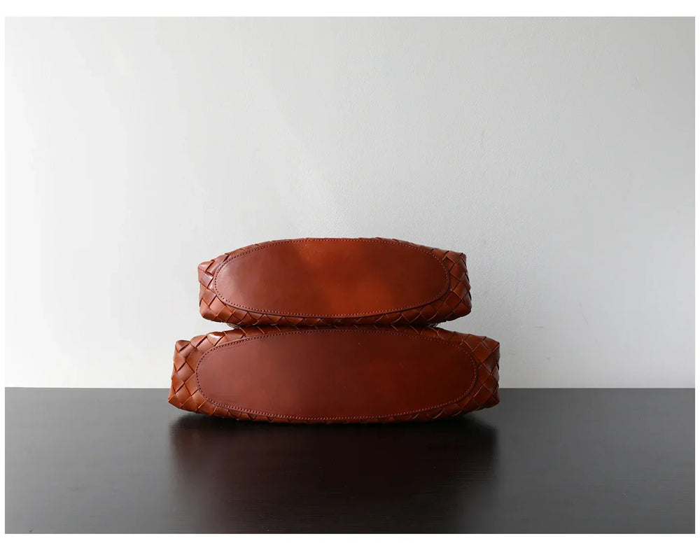 Bottom view of two brown woven leather hobo bags with trapezoidal shape on a dark surface
