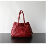 Red woven leather hobo shoulder bag with long handles on a dark table, trapezoidal shape