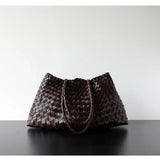 Dark brown woven leather hobo trapezoid shoulder bag with long handles on black surface