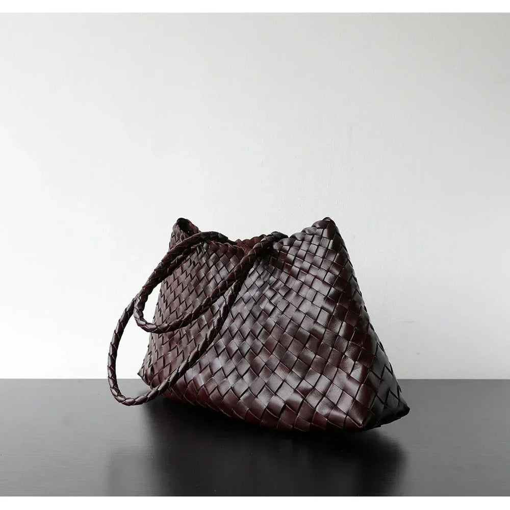 Woven leather hobo trapezoidal shoulder bag with long handles on a dark surface.
