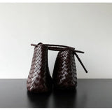 Side view of two dark brown woven leather hobo bags with long handles on black surface