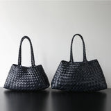 Woman holding black woven leather hobo bag with dual handles, stylish and trapezoidal shape black