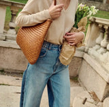 Woman carrying woven leather hobo tote bag and flowers, wearing casual jeans outdoors