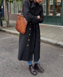 Woman wearing black trench coat and jeans carries a brown woven leather tote bag on street