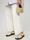Woman holding beige lambskin leather mini Boston bag, wearing white pants and sandals
