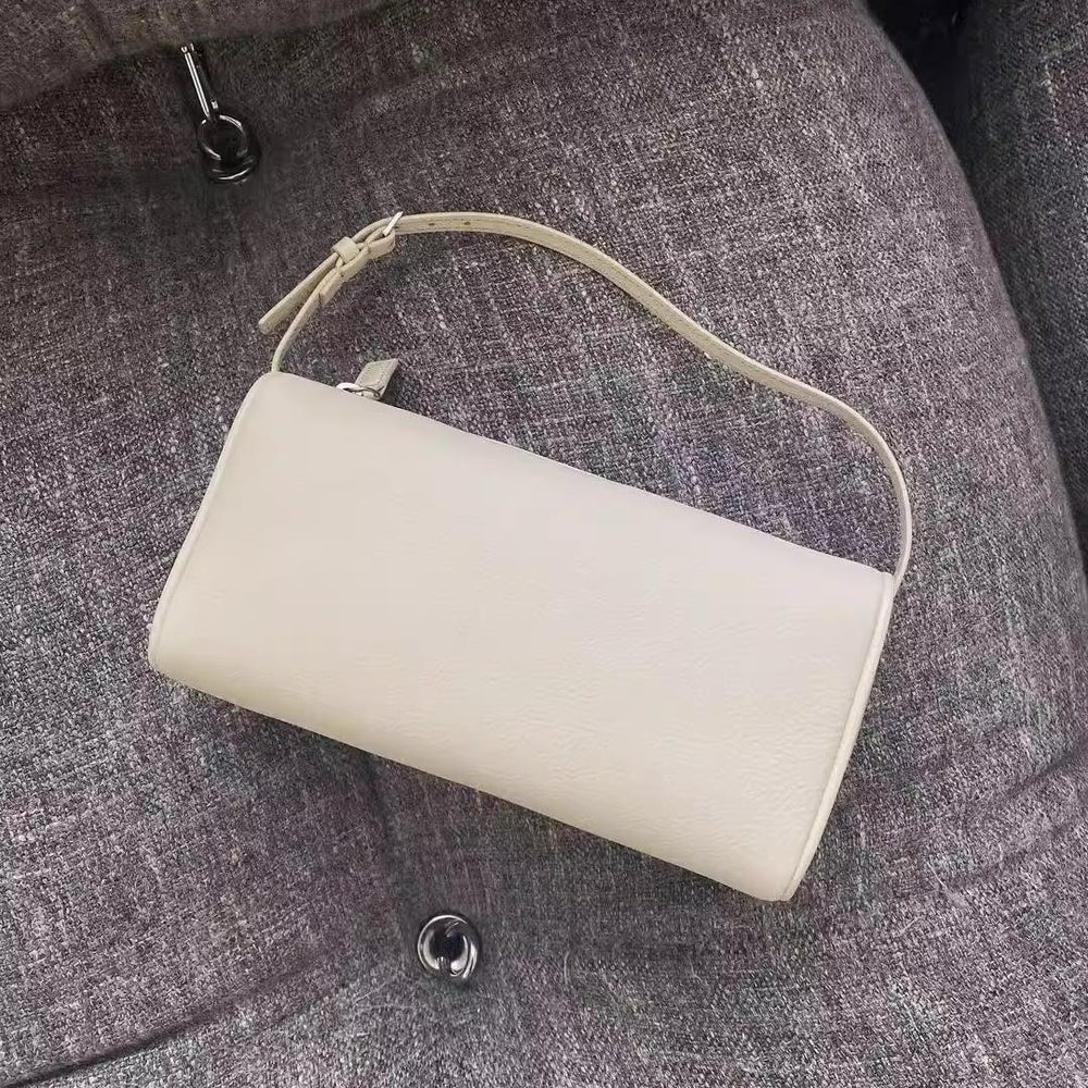 Minimalist white lambskin leather mini Boston bag with shoulder strap on gray fabric chair