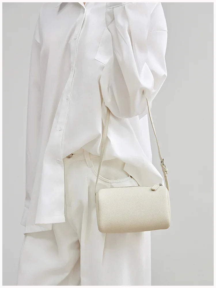 Minimalist beige lambskin leather crossbody mini bag with box shape, worn over white outfit