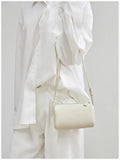 Minimalist beige lambskin leather crossbody mini bag with box shape, worn over white outfit