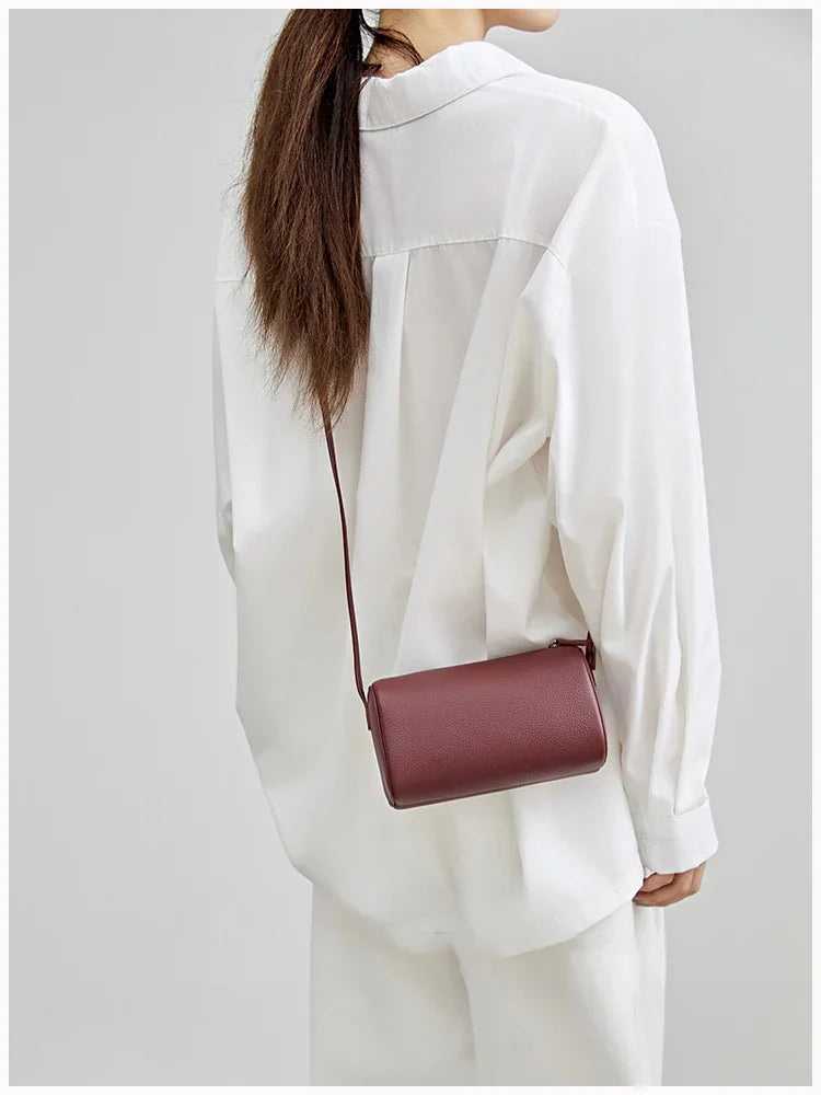 Minimalist brown lambskin leather crossbody bag worn over a white oversized shirt