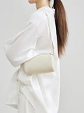 Woman wearing minimalist cream lambskin leather mini shoulder bag with adjustable strap