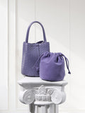 Purple woven lambskin leather bucket bag and matching suede pouch on white pedestal