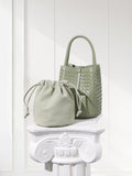 Small sage green lambskin leather bucket bag and handwoven purse on white pedestal
