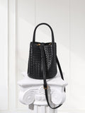 Black woven lambskin leather bucket bag with shoulder strap on white pedestal