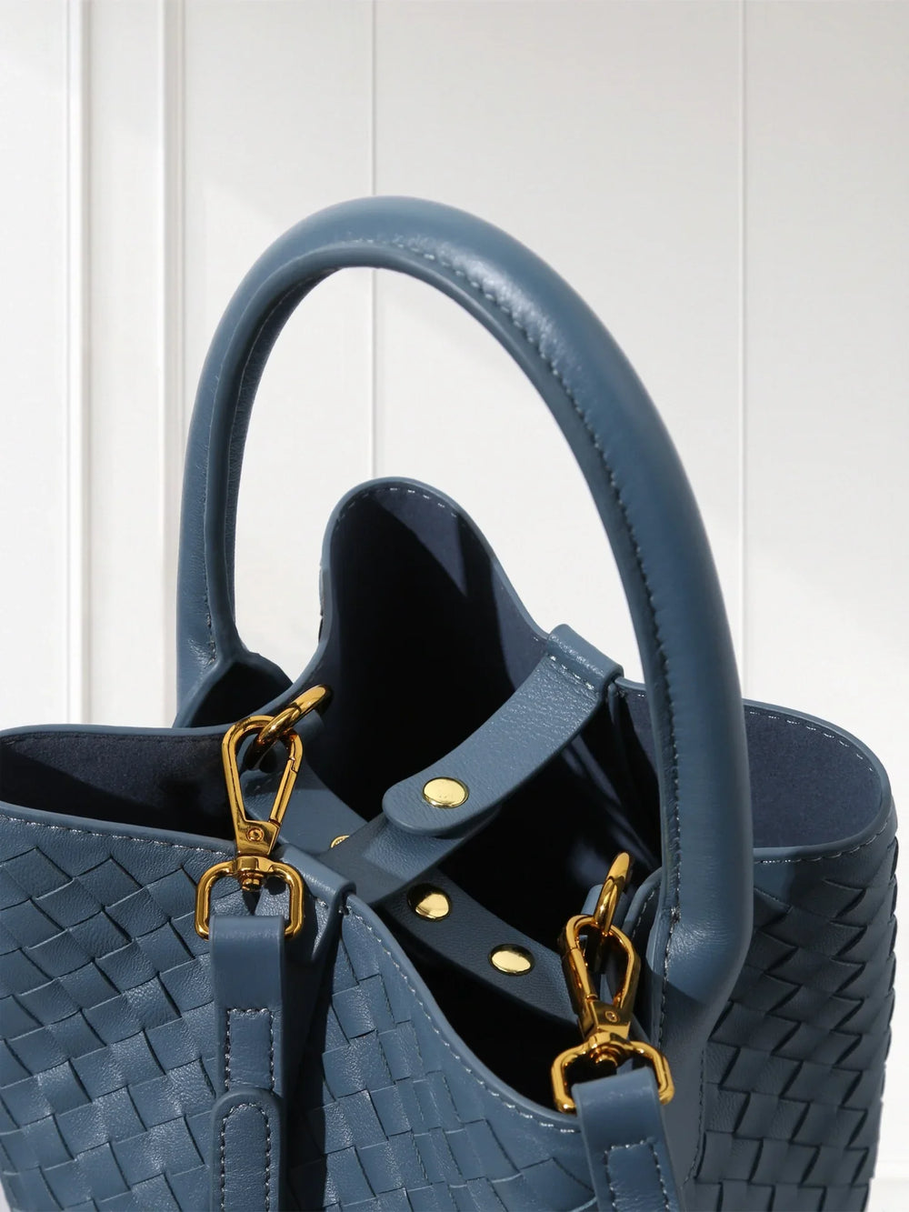 Blue lambskin leather woven bucket bag with gold hardware and top handle on white background