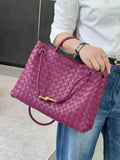 Purple woven lambskin leather shoulder bag with gold metal buckle, held by woman in jeans and white shirt.