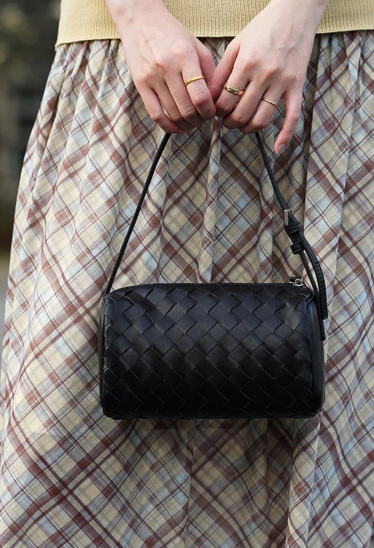 Woman holding a black woven lambskin leather mini Boston bag with shoulder strap