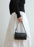 Woman holding a black woven lambskin leather mini Boston bag with shoulder strap.