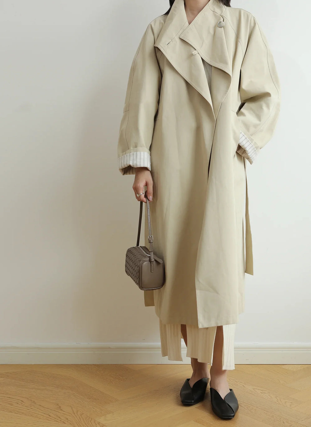 Woman in beige trench coat holding a taupe lambskin woven leather mini shoulder bag