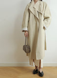 Woman in beige trench coat holding a taupe lambskin woven leather mini shoulder bag