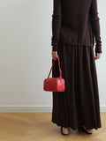 Woman holding a small red woven lambskin leather shoulder bag, wearing a dark brown dress