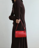 Woman holding a red woven lambskin leather mini Boston bag with shoulder strap
