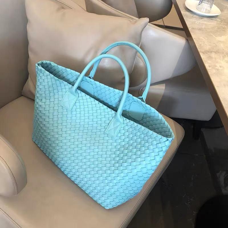Large light blue handwoven vegan leather tote bag with double handles on a beige chair