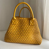 Large handwoven vegan leather tote bag in yellow with double handles, displayed indoors.