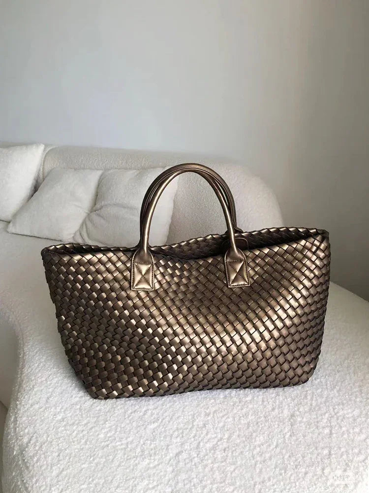 Large handwoven vegan leather tote bag in onyx with double handles on a white sofa.