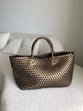 Large handwoven vegan leather tote bag in onyx with double handles on a white sofa.