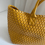 Large woven vegan leather tote bag in mustard yellow with double handles on white background