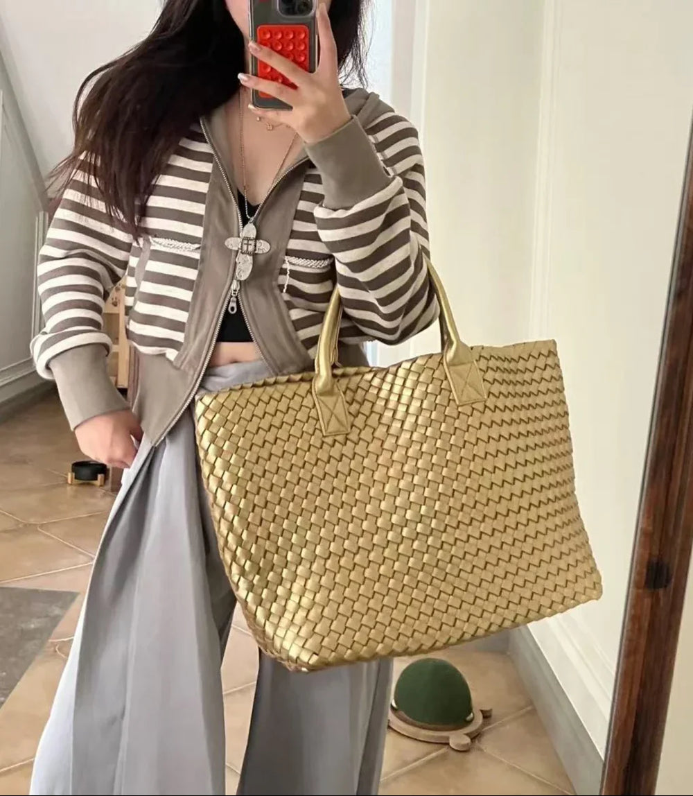 Woman holding large handwoven vegan leather tote bag in gold, perfect for weekend travel.