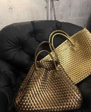 Two large handwoven vegan leather tote bags in gold and bronze on a black cushioned chair