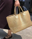 Handwoven gold vegan leather tote bag with double handles carried outdoors
