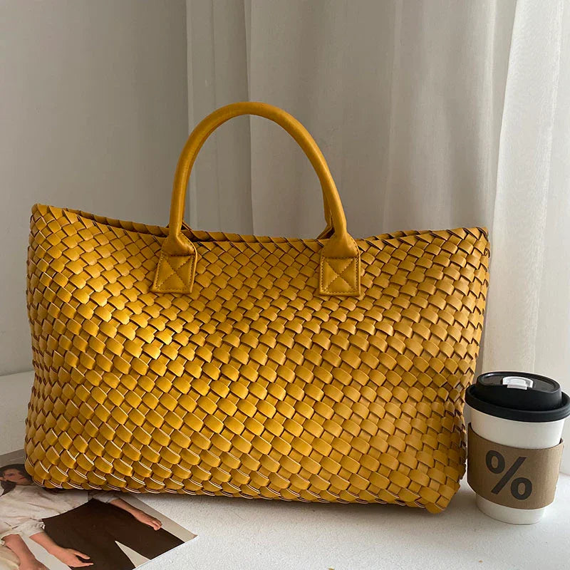 Yellow handwoven vegan leather tote bag with top handles, placed beside a coffee cup indoors.