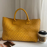 Yellow handwoven vegan leather tote bag with top handles, placed beside a coffee cup indoors.