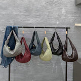 Five woven lambskin leather knotted handbags in assorted colors hanging on a clothing rack.