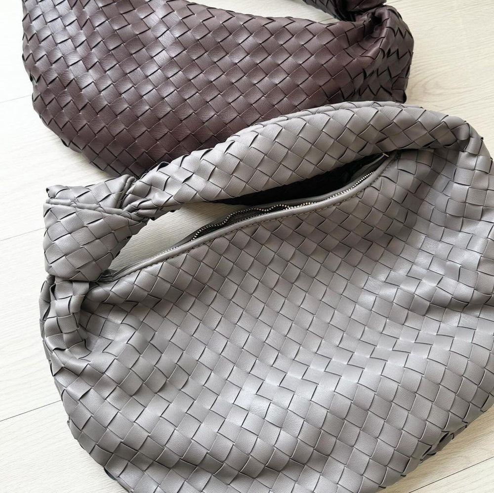 Two large woven lambskin leather handbags with knotted straps in brown and grey on light wood floor