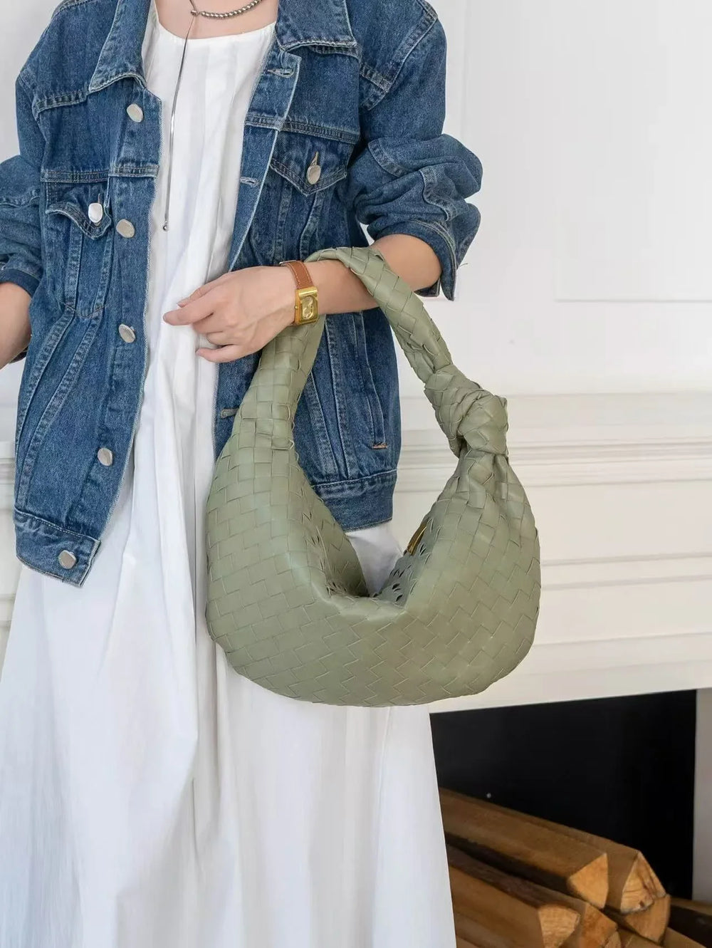 Woman holding large green woven lambskin leather knotted handbag, wearing denim jacket and white dress