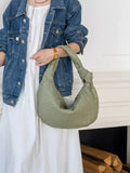 Woman holding large green woven lambskin leather knotted handbag, wearing denim jacket and white dress