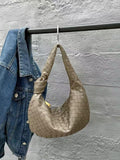 Taupe woven lambskin leather knotted handbag hanging beside a blue denim jacket