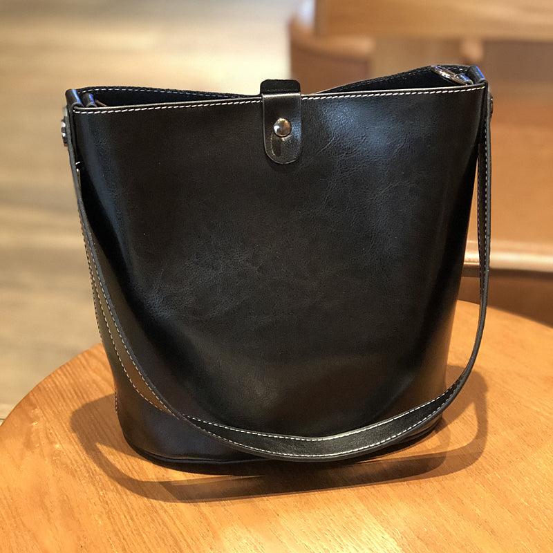 Brown leather bucket bag with shoulder strap and snap closure on wooden table